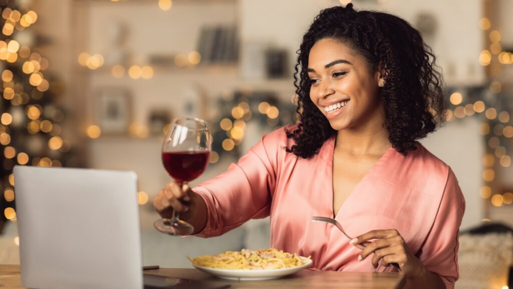 lady raising her wine glass in a toast as she eats her favourite dinner with her long distance boyfriend