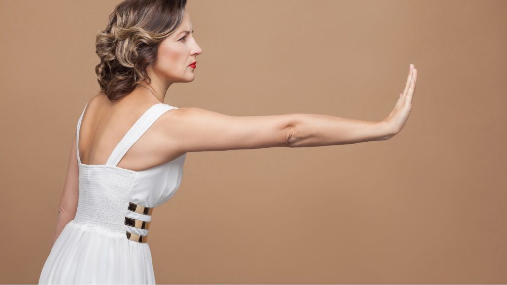 lady wearing a white gown on brown background making a gesture of rejection