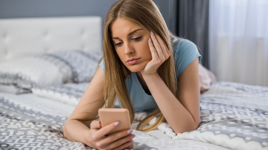 lady wearing blue polo on her bed waiting for her partner's message to drop