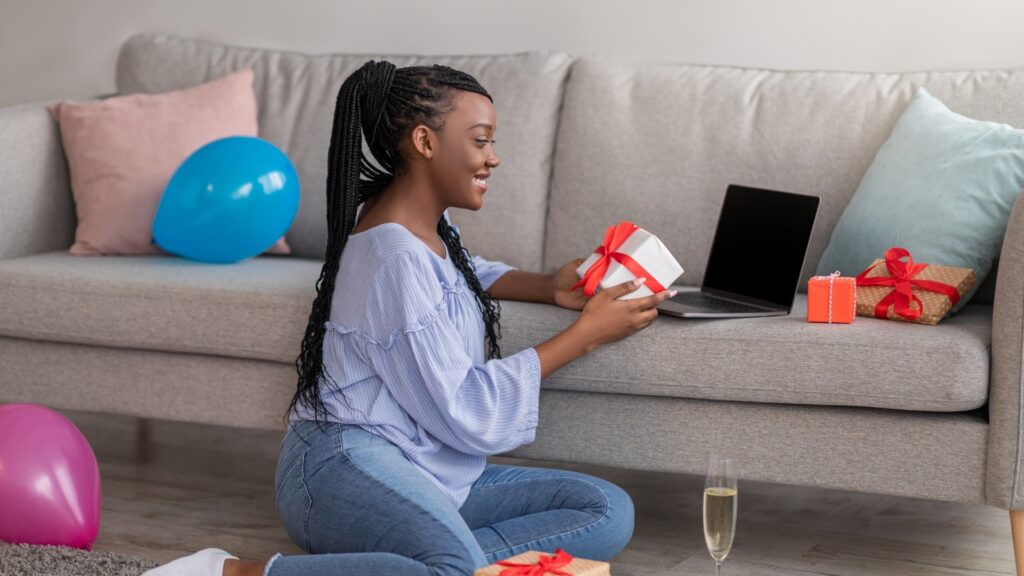 black woman sitting on the floor while on video call with her long distance partner showing him the care package she receivedfrom him