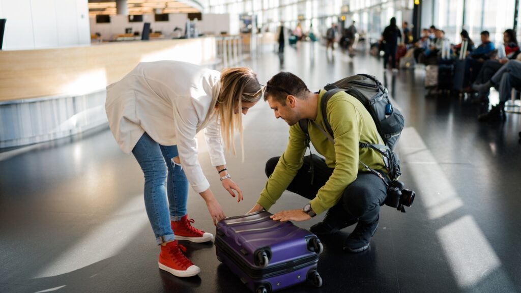 man trying to help his long distance partner zip her bag at the airport